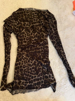 Leopardmönstrad mesh topp Intimissimi - Snygg långärmad topp från Intimissimi i transparent mesh med leopardmönster. Toppen har en tight passform och är perfekt för att sticka ut. Materialet är mjukt och stretchigt, vilket gör den bekväm att bära. Perfekt för dig som gillar djurmönstrat!