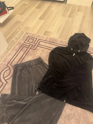 Mjukis-set från Gina Tricot XS - Säljer ett mysigt loungewear-set från Gina Tricot i storlek XS. Setet består av en svart hoodie med dragkedja och huva samt ett par grå mjukisbyxor med resår och dragsko i midjan. Båda delarna är i mjuk velour som känns superbekväm.