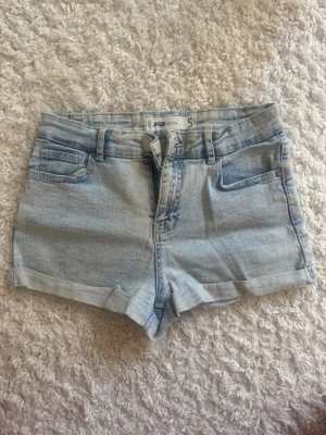 Ljusblå denimshorts från F3 Sister - Snygga ljusblå denimshorts från F3 Sister med klassisk femficksdesign, uppvikta benslut och bälteshällor. Perfekta för varma dagar och enkla att matcha med allt. Dragkedja och knapp framtill.