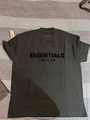 Svart Essentials T-shirt Fear of God - Svart T-shirt från Fear of God Essentials med stor logga på bröstet. Klassisk rund hals och korta ärmar. Tillverkad i mjuk bomull för en skön och avslappnad stil.