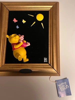 JIE Charmiga 3D-tavlor med Nalle Puh & Nasse och Tiger,  Disney - Charmiga 3D-tavlor med Nalle Puh & Nasse och Tiger tillverkad av JIE Gantofta i Sverige. Ramen är i trä och motivet är monterat på en svart bakgrund. En fin detalj för barnrummet eller för Disney-samlaren. På en av tavelramarna (Puh & Nasse med solen) har ramen en större springa i hörnen, se bilder.  I nedre delen av ramen på Tigers tavla är det ett litet hål, se bild.  Mått:   26,5 x 31,5cm 15x15 cm 36,5x21,5 cm  Priset är för alla tavlorna!