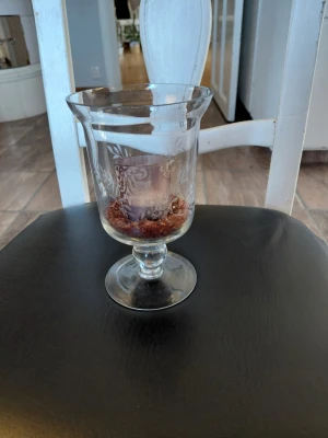 Glaslykta med graverat mönster - Snygg glaslykta med graverat bladmönster och fot. Inuti finns ett lila värmeljushållare och dekorativa bruna stenar. Perfekt som dekoration i hemmet för mysig stämning.