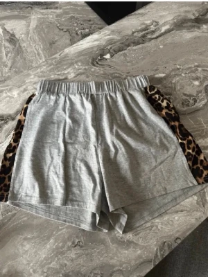 Grå shorts med leoparddetaljer - Grå shorts med elastisk midja och leopardmönstrade paneler på sidorna. Sköna och avslappnade, perfekta för en chill look. Tillverkade i mjuk bomullsmix som känns bekväm mot huden.