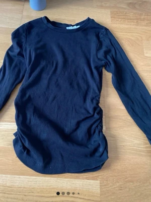 Svart långärmad ribbad tröja - En svart långärmad tröja med ribbad struktur och rund halsringning. Tröjan har en enkel och stilren design, perfekt att matcha med jeans eller kjol. Materialet ser ut att vara mjukt och stretchigt för en bekväm passform.