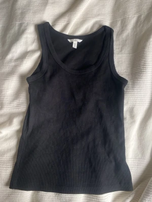 Svart ribbad linnetopp H&M - Säljer en svart ribbad linnetopp från H&M. Toppen är ärmlös med rund halsringning och har en slim passform. Perfekt att styla till jeans eller kjol för en enkel och snygg look.