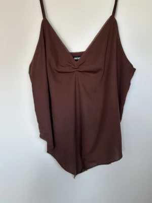 Brun linnetopp med v-ringning - Säljer en brun linnetopp från Bik Bok med smala axelband och snygg v-ringning framtill. Toppen har en lös passform och är tillverkad i ett lätt och mjukt material, perfekt för varma dagar.