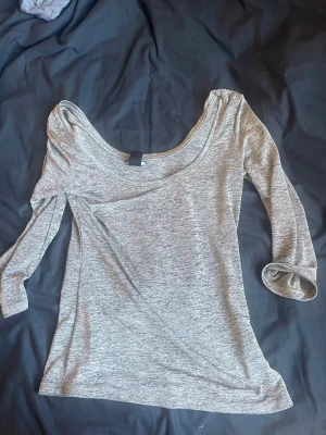 Grå långärmad topp med bred ringning - Säljer en enkel och stilren grå långärmad topp med bred ringning. Toppen har en mjuk och stretchig känsla, perfekt för en avslappnad look. Passformen är normal och materialet känns som bomull eller en bomullsblandning.