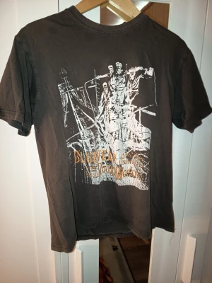 Mörk t-shirt Bluewear Rough Working - Cool mörk t-shirt från Bluewear med stort tryck på ryggen som visar arbetare och texten 'Rough Working'. T-shirten har korta ärmar och en klassisk passform. Perfekt för dig som gillar streetwear med industriell känsla.