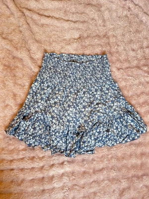 Blommig blå volangkjol från 157 - Supersöt blå kortkjol från 157 med vitt blommönster och volangkant. 