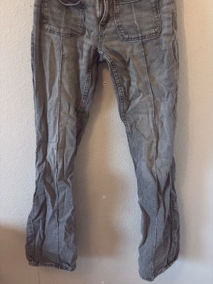 Gråa bootcut jeans - Säljer ett par gråa jeans med raka ben och stora framfickor. Jeansen har en avslappnad passform och synliga sömmar framtill som ger en cool vintagekänsla. Perfekta för en chill och trendig look. För mer frågor är det bara att dma💞