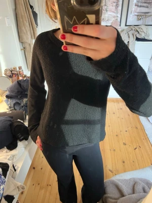 Svart stickad tröja med rund hals - En enkel och stilren svart stickad tröja med rund halsringning och långa ärmar. Tröjan har en rak passform och ribbstickade muddar vid nederkant och ärmslut. Perfekt att matcha med jeans eller kjol för en clean look.