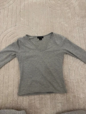 Grå v-ringad topp - Grå långärmad topp med v-ringning. Modellen är enkel och figurnära, perfekt att matcha med jeans eller kjol. Tillverkad i mjukt material som känns skönt mot huden.