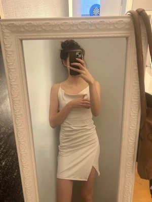 Vit kort klänning med snörning - Säljer en vit kort klänning med smala axelband och snygg snörning i ryggen. Klänningen har en slits på sidan och är figurnära med en enkel, stilren design. Perfekt för dig som gillar minimalistiskt och trendigt mode.