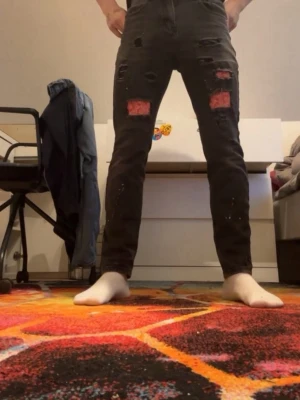 Svarta skinny jeans med röda slitningar - Säljer ett par svarta skinny jeans med röda slitningar och hål på båda benen. Jeansen har en tight passform och är dekorerade med vita färgstänk för en edgy look. Perfekta för dig som gillar streetstyle och vill sticka ut.