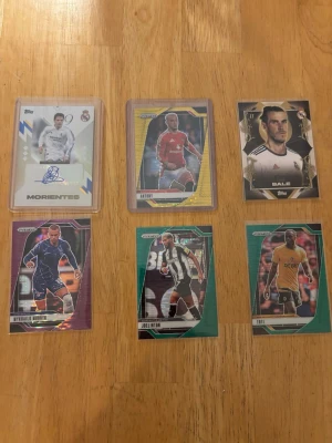 Fotbollskort Topps och Panini - Säljer en samling fotbollskort från Topps och Panini med spelare som Morientes, Antony, Bale, Hybril Monte, Joelinton och Ibil. Kort i olika färger och design, vissa med autograf och holografiska detaljer. Perfekt för dig som gillar fotboll och samlarobjekt.