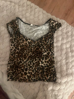 Leopardmönstrad topp från Nelly - Säljer en leopardmönstrad topp från Nelly med korta ärmar och v-ringad hals. Tunn och stretchig modell som sitter snyggt på kroppen. Perfekt för dig som vill sticka ut med ett djurmönster i brunt och svart.