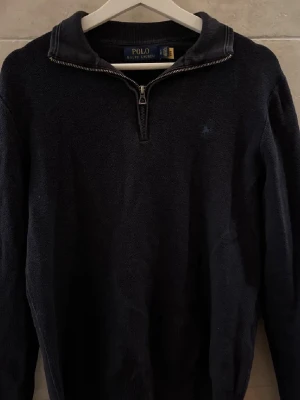  Halvzip-tröja från Polo Ralph Lauren - Klassisk marinblå långärmad tröja från Polo Ralph Lauren med halvzip och krage. Tröjan har diskret broderad logga på bröstet och är tillverkad i ett stickat material. Perfekt för en stilren och avslappnad look.