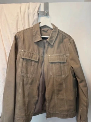 Beige jeansjacka från ASOS DESIGN - Snygg beige jeansjacka från ASOS DESIGN med dragkedja framtill, två bröstfickor med lock och markerade sömmar. Jackan har klassisk krage och är helfodrad för extra komfort. Perfekt för dig som gillar stilren och enkel design.