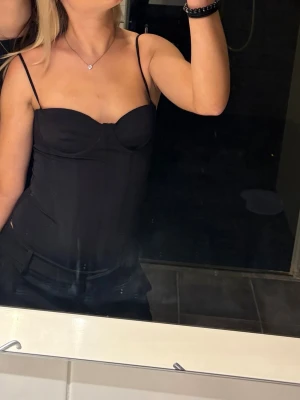 Svart body. med tunna axelband - Snygg svart body med tunna axelband och markerade kupor. Toppen har en tight passform och ger en stilren och trendig look. Perfekt att matcha med både jeans och kjol för en cool outfit.