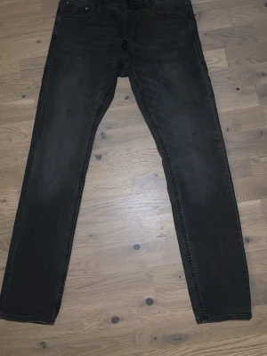 Grå slim fit jeans från Jack & Jones - Snygga grå slim fit jeans från Jack & Jones, modell 'Slim Glenn'. Jeansen har klassisk femficksdesign, knappgylf och diskreta slitningar för en trendig look. Perfekta för dig som gillar en smalare passform och vill ha ett par stilrena vardagsjeans.