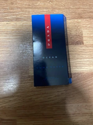 Prada Luna Rossa Ocean parfymprov - Säljer ett parfymprov av Prada Luna Rossa Ocean. Förpackningen är blå med en röd detalj och flaskan är genomskinlig med sprayfunktion. En fräsch och modern doft från ett exklusivt märke, perfekt att testa eller ha med sig i väskan.