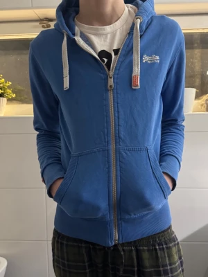 Superdry Hoodie - Hej! Jag säljer min blå tröja från Superdry i storlek M. Den är i fint skick och lätt att matcha med olika outfits. Tyvärr kan jag inte sälja den via Plick, men jag kan mötas upp när som helst. Hör gärna av dig vid intresse!