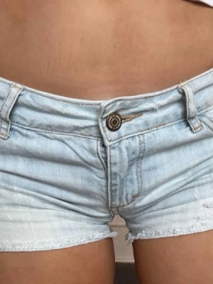 Ljusblå denimshorts med rå kant - Snygga ljusblå jeansshorts i klassisk femficksmodell med rå, fransig kant nertill. Shortsen har knapp och dragkedja framtill samt bälteshällor. Perfekta för varma dagar och ger en avslappnad vibe.