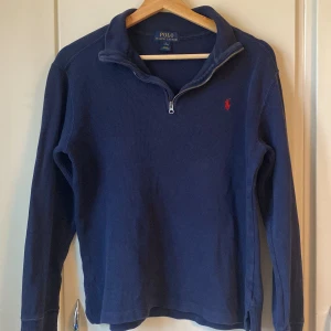Ralph Lauren Marinblå Half zip - Marinblå stickad äkta tröja från Polo Ralph Lauren med halv dragskedja och klassisk röd broderad logga på bröstet. Tröjan har lång ärm och ribbade muddar. 12-15 år. L i barn storlek.