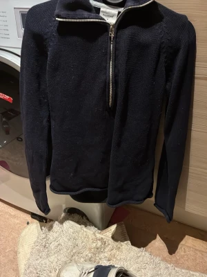 Mörkblå stickad tröja med halv dragkedja - Säljer en mörkblå stickad tröja med hög krage och halv dragkedja framtill. Tröjan har lång ärm och är tillverkad i ett mjukt stickat material. Perfekt för lager på lager och enkel att matcha med olika outfits.