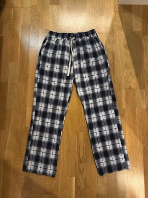 Rutiga pyjamasbyxor i bomull - Mysiga pyjamasbyxor med svart, vitt och grått rutmönster. Byxorna har resår i midjan och dragsko för skön passform. Perfekta för chillkvällar hemma. Tillverkade i mjuk bomull som känns skön mot huden.