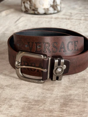 Vintage Versace skärp   - Vintage skärp från Versace i äkta skinn med präglad logga längs hela bandet. Spännet är i silverfärgad metall med Versace-detaljer och Medusa-huvud. Perfekt accessoar för att lyfta din outfit.