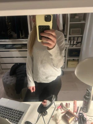 Ljusgrå stickad tröja - En enkel och stilren ljusgrå stickad tröja med rund halsringning och långa ärmar. Tröjan har ribbade muddar vid ärmslut och nederkant. Perfekt att matcha med jeans eller kjol för en avslappnad look.