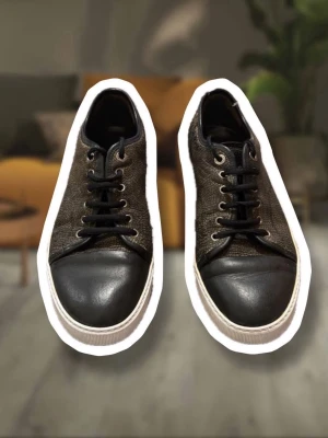 Sneakers med crocodil läder från lanvin - OBS st 42 men passar 43!                             Snygga svarta sneakers med texturerad ovandel och tå i slätt läder. Skorna har svarta skosnören, vita sulor och metallfärgade öljetter. Perfekta för dig som gillar en stilren och urban look.