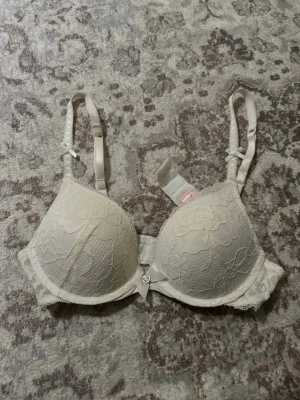 vit push-up bh med spetsdetaljer - Snygg vit push-up bh med vadderade kupor och vacker spets över hela framsidan. Justerbara axelband med små rosetter och en liten dekorativ rosett med strass framtill. Klassisk hakknäppning bak och mjukt material för extra komfort. Oanvänd! 