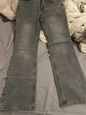 Gråa bootcut jeans med medel midja  - Säljer ett par gråa bootcut jeans med medel midja och klassisk femficksdesign. Jeansen har en snygg tvättad look och vida ben som ger en retrovibe. Perfekta för dig som gillar en avslappnad men trendig stil.