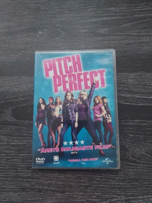 Pitch Perfect DVD - Pitch Perfect DVD med blå omslag och rosa text. Filmen är en musikalisk komedi med flera karaktärer på framsidan. Omslaget har citat och bilder från filmen samt information om handlingen på baksidan. Perfekt för filmkvällar och samlingar.