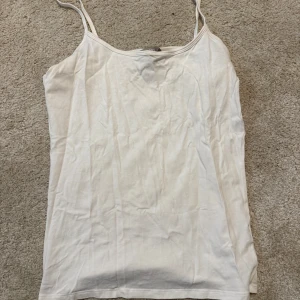 Vit linnetopp från Åhléns - Säljer en enkel och stilren vit linnetopp från Åhléns i storlek M. Toppen har tunna axelband och ärmlös design, perfekt för varma dagar. Materialet känns mjukt och lätt mot huden, vilket gör den superbekväm att bära.