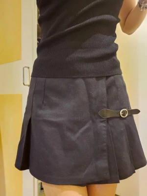 Mörkblå kortkjol med bältdetalj - ❗️Skriv innan köp❗️Kort mörkblå kjol med veck och 2 dekorativa bältdetaljer. Går att justera vid midjan med knappar och bältedetaljer är funktionella. Har köpt hos brandy melville och använt ett fåtal ggr. 