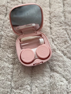 Rosa linsfodral med spegel - Säljer ett smidigt rosa linsfodral i plast med spegel i locket. Inuti finns behållare för vänster och höger lins, en liten flaska för vätska samt pincett. Perfekt att ha med i väskan för enkel hantering av linser.