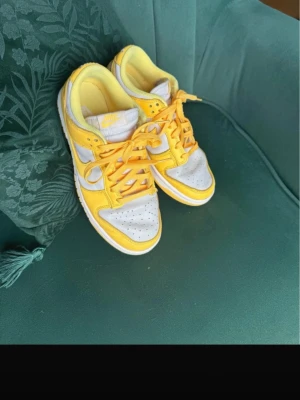 Nike Dunk Low gul och vit - Säljer ett par Nike Dunk Low sneakers i fräscha färger. Skorna har vit bas med gula overlays, gula skosnören och vit sula. Klassisk Nike Swoosh i gult på sidan och perforerad tåbox för extra ventilation. Perfekta för dig som vill sticka ut med färg!