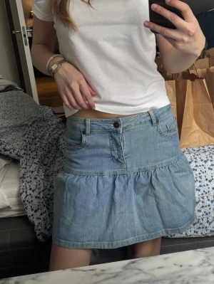 Blå volangkjol i denim - Snygg blå jeanskjol med volang och klassiska fickor fram. Lågmidjad. 