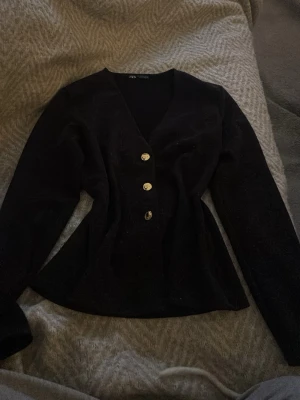 Svart kofta med guldknappar från Zara - Stilren svart kofta från Zara med figurnära passform och djup V-ringning. Framsidan har tre dekorativa guldknappar som ger en snygg detalj. Långärmad modell. Nypris 300kr💕💕