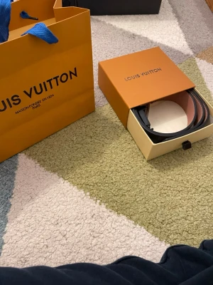 L*****n rutigt bälte svart/grå - Säljer ett  bälte i klassiskt rutigt mönster i svart och grått med svart LV-spänne. Bältet har en brun insida och levereras med originalförpackning och påse. Perfekt accessoar för att lyfta din outfit.