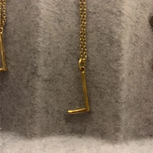Guldigt halsband med minimalistisk stav - Snyggt halsband i guldfärg med en tunn kedja och en minimalistisk stavformad hängare. Perfekt för dig som gillar stilrena och moderna accessoarer. Halsbandet har en enkel och elegant design som passar till många olika looks.