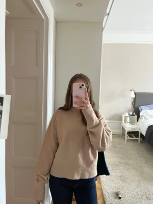 Beige stickad tröja med rund hals - En enkel och stilren beige stickad tröja med rund hals och långa ärmar. Tröjan har en rak passform och ribbstickade muddar vid ärmslut och nederkant. Perfekt för lager-på-lager och passar till jeans eller kjol.