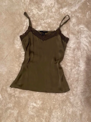 Olivgrön linnetopp med spetsdetaljer - Säljer en snygg olivgrön linnetopp i äkta silke (98%) med tunna axelband och dekorativ spets längs urringningen 🌸🫒 Det står storlek 40/10 men skulle säga S/M då den passar mig bra som S. skriv om du har frågor!