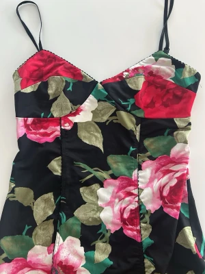Blommig svart klänning med smala band - Snygg svart klänning med stora blommor i rött, rosa och vitt samt gröna blad. Klänningen har smala axelband, v-ringad urringning och figurnära passform. Pris kan diskuteras , öppen rygg 💛⭐️