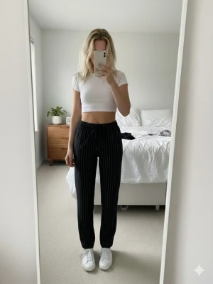 Svarta randiga byxor med snörning - Säljer ett par svarta byxor med vita tunna ränder och snörning i midjan. Byxorna har hög midja, resår i midjan och smal passform. Materialet känns mjukt och stretchigt, perfekt för en chill och snygg look.