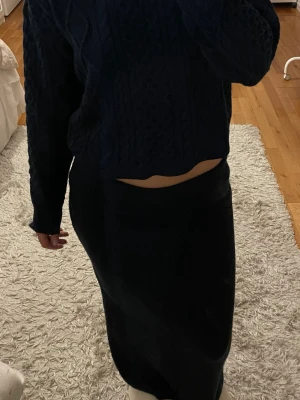 Mörkblå stickat set - Mysig mörkblå stickat set med en tröja med hög hals och långa ärmar och en stickad kjol. Tröjan har ett klassiskt stickat mönster och ribbade muddar vid ärmslut och nederkant. 