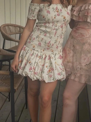 Blommig offshoulder kortklänning H&M - Supersöt kortklänning från H&M med offshoulder och volangig kjol. Klänningen är vit med blommigt mönster i rosa, gult och grönt. Smockad överdel som sitter tajt och fluffig kjol. Perfekt för sommarens alla tillfällen!